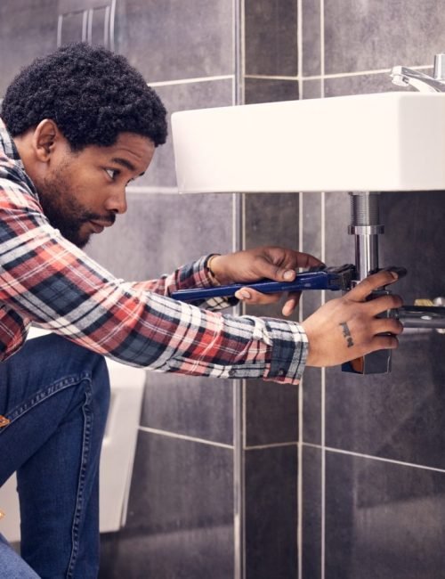 black-man-plumber-and-maintenance-in-bathroom-fixing-sink-pipe-with-wrench-and-plumbing-industry--e1705240801490